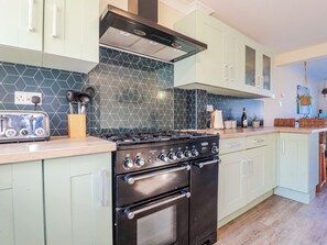 A kitchen with light green cabinets, a black stove, a hexagonal tile backsplash, and a wooden countertop. - 3A Grannys Lane (Perranporth)