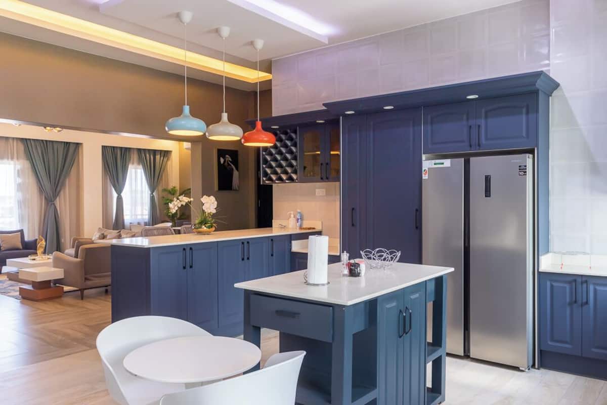 Una cocina moderna con armarios azul oscuro, un refrigerador de acero inoxidable e iluminación colgante.