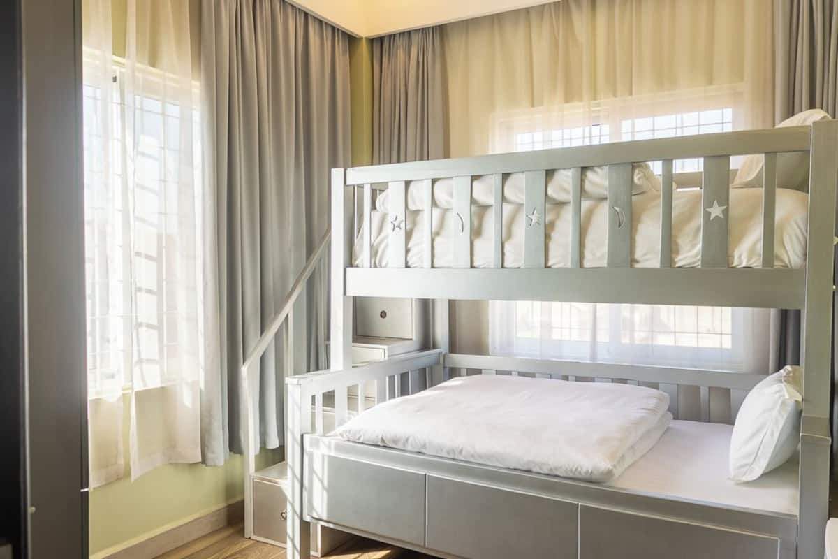 Una litera con una cama inferior, una mesita de noche y una ventana con cortinas.
