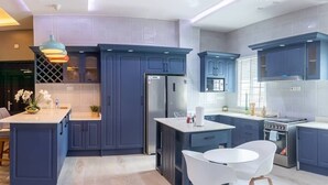 A modern kitchen with dark blue cabinets, a central island, white chairs, and a built-in oven. - BELLEVIEW APARTMENTS (Kampala)
