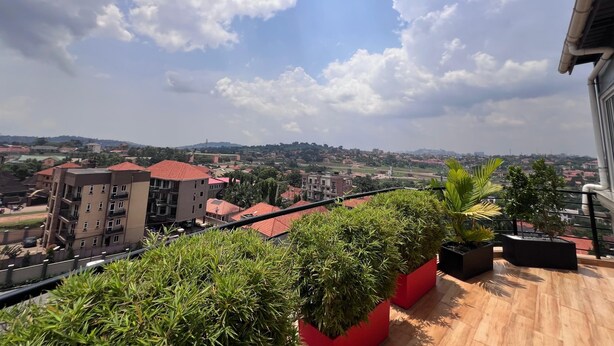 A balcony with potted plants, a view of a residential area, and a clear sky. - BELLEVIEW APARTMENTS (Kampala)