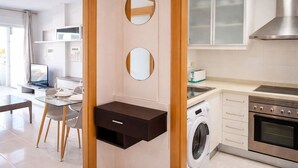 Eine moderne Küche mit Einbauwaschmaschine, einem Essbereich mit Glastisch und einem großen Fenster.