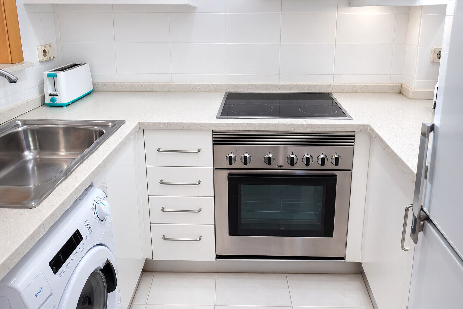 Una cocina compacta con horno integrado, lavadora y tostadora.