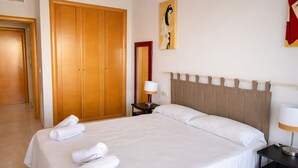 Ein Hotelzimmer mit einem großen Bett, einem Holzschrank, einem Nachttisch, einer Lampe und einem Gemälde an der Wand.