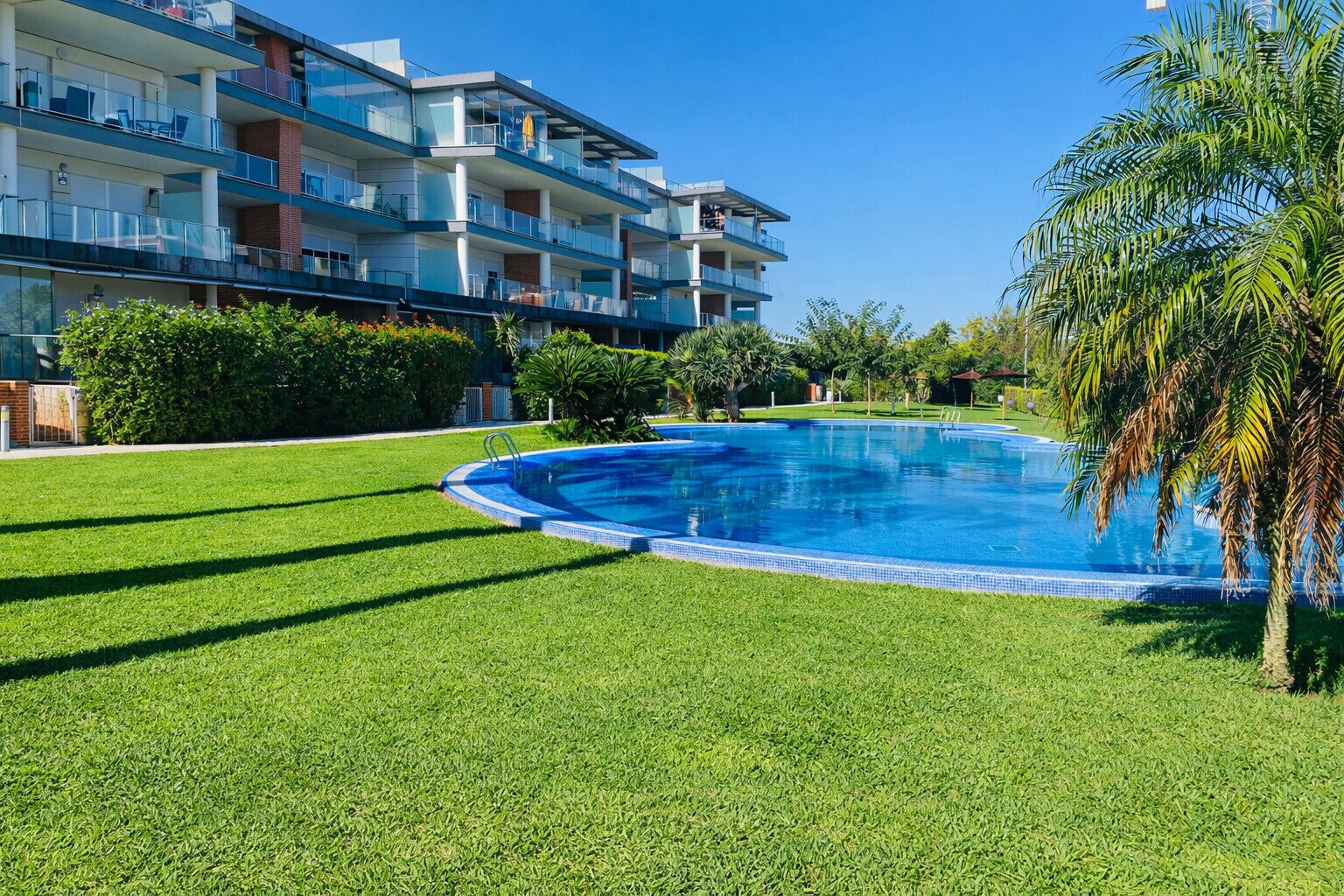Una piscina circondata da prato curato, con un edificio a più piani sullo sfondo.