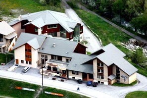 A multi-story building with a sloped roof, a parking area, and a road curving around it.