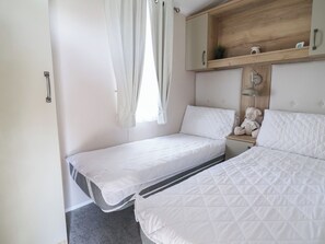 A bedroom with two beds, a wooden shelf above, and a bedside lamp. - Elsie Rose (Ruthin)