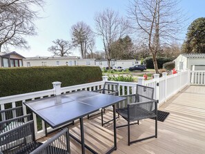 Eine Terrasse mit Tisch und Stühlen, umgeben von einem weißen Zaun, mit Blick auf eine Wohngegend mit Häusern und geparkten Autos.