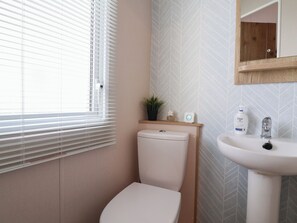 Ein Badezimmer mit Toilette, Waschbecken, Spiegel und einem Fenster mit Jalousien.