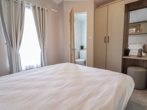 Ein Schlafzimmer mit Bett, Kleiderschrank, Badezimmer und einem kleinen Regal mit einer Pflanze.
