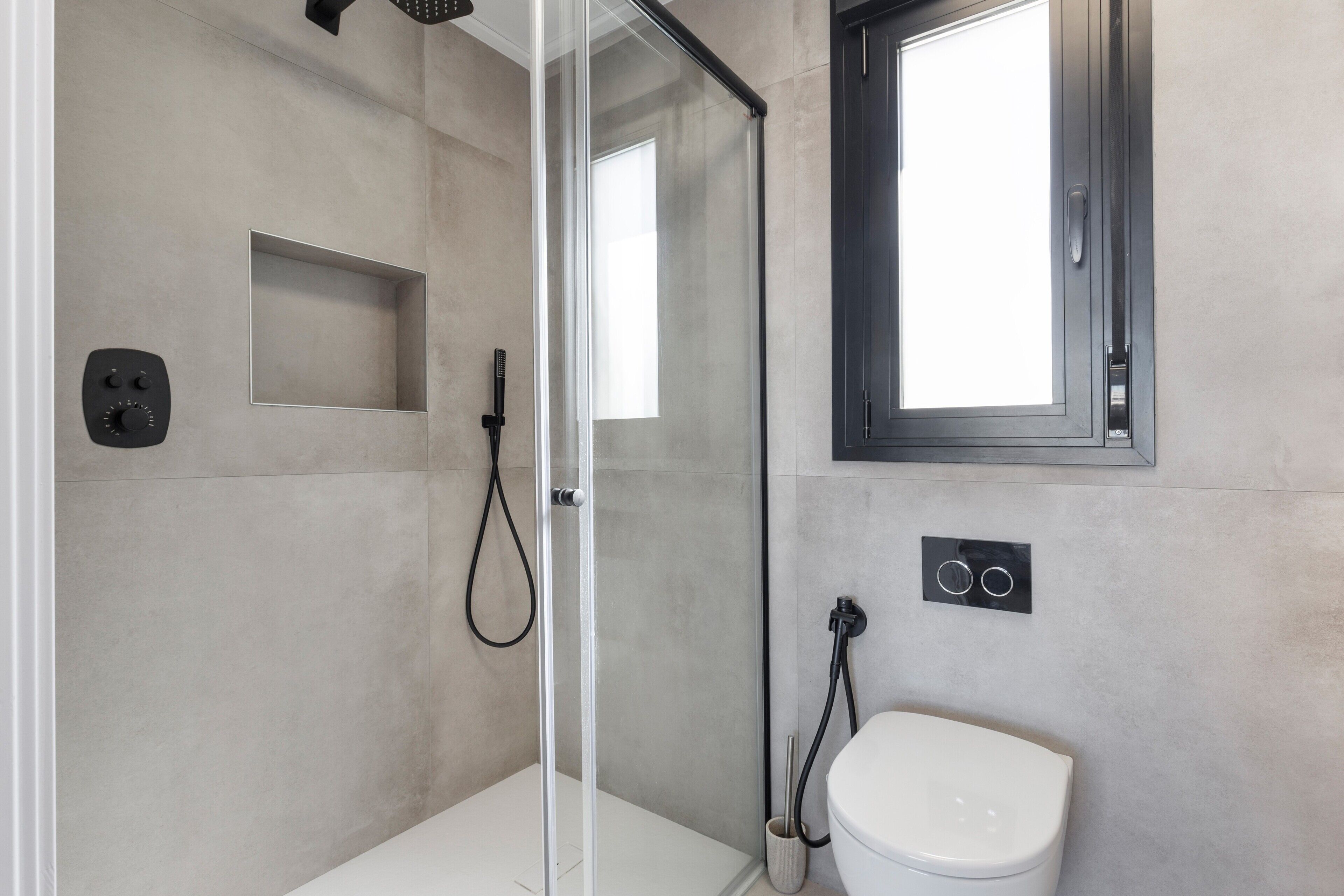 Een moderne badkamer met een douchecabine van glas, een toilet en een raam.