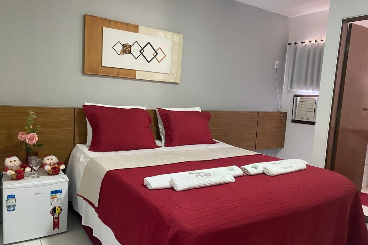 A hotel room with a bed, a minibar, a wall-mounted artwork, and a door.