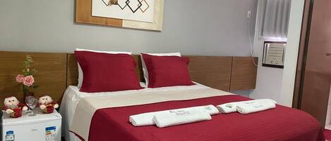 A hotel room with a bed, a minibar, a wall-mounted artwork, and a door.