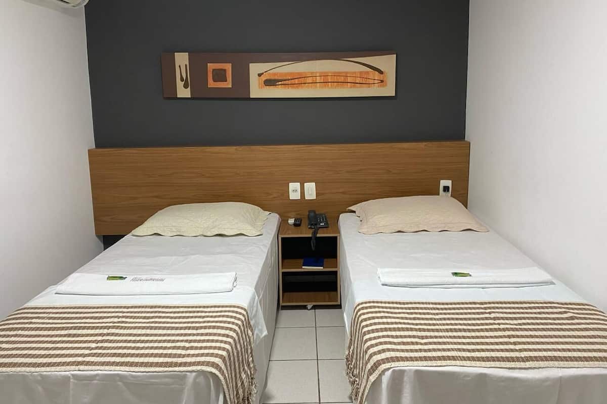 A twin room with two beds, a wooden headboard, a wall-mounted artwork, a telephone, and a small shelf.
