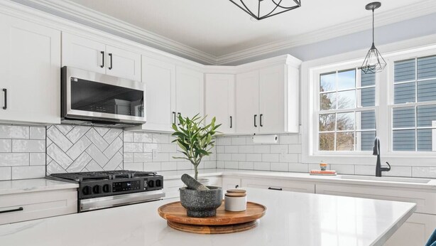 A modern kitchen with white cabinetry, a built-in stove, a large island with a stone mortar and pestle, and a hanging light fixture. - Luxury Modern Boston Townhome w/ Parking! (Boston)