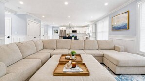 A living room with a sectional sofa, a coffee table with a tray, and a kitchen in the background. - Luxury Modern Boston Townhome w/ Parking! (Boston)