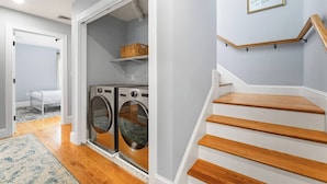 A laundry room with two front-loading washers and dryers, a wooden floor, and a staircase with a wooden handrail. - Luxury Modern Boston Townhome w/ Parking! (Boston)