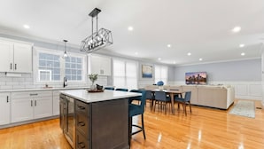 A modern kitchen with white cabinets, a wooden island, and a dining area with blue chairs. - Luxury Modern Boston Townhome w/ Parking! (Boston)