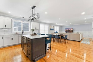 Una cocina moderna con armarios blancos, una isla de madera y un comedor con sillas azules.