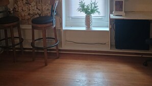 A living room with a wooden floor, a window with blinds, a chair, a table, and shelves with various items. - Tranquil 1-bedroom cottage with AC in charming Augusta near the Masters! (Augusta)