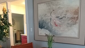 A dining area with a wooden table and benches, a framed abstract painting on the wall, and a potted plant on the table. - Tranquil 1-bedroom cottage with AC in charming Augusta near the Masters! (Augusta)