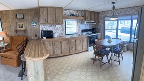 A kitchen with wooden cabinets, a dining area with chairs, a microwave, and a sink. - 2-bedroom mobile home in Henderson (Henderson)