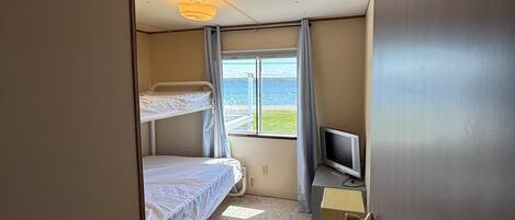 Ein Hotelzimmer mit Etagenbett, Schreibtisch und Fernseher, sowie ein Fenster mit Meerblick.