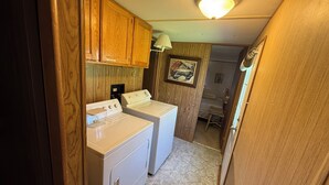 A compact laundry room with wooden cabinets, a washing machine, a dryer, and a ceiling light fixture. - 2-bedroom mobile home in Henderson (Henderson)
