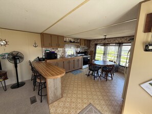 A compact kitchen with a central island, a dining table with chairs, and a view of the outdoors through a window. - 2-bedroom mobile home in Henderson (Henderson)