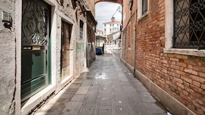 Un estrecho callejón flanqueado por edificios de ladrillo, una puerta verde y un toldo blanco.