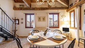 Comedor con una mesa redonda para dos, una araña y vistas a edificios a través de amplios ventanales.