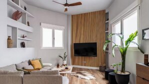 Un salon moderne avec un canapé, un téléviseur, un mur recouvert de panneaux en bois et des plantes en pot.