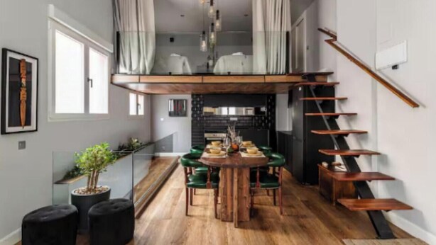 Un coin repas avec une table et des chaises en bois, un escalier et une cuisine en arrière-plan.