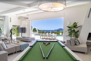 A pool table in a modern living room with a view of the sea.