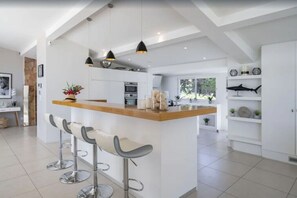 A modern kitchen with a central island, bar stools, pendant lighting, and a view of the outdoors. - FRGK Contemporary Luxury Villa Panoramic Sea View (Cannes)