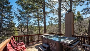 Ein Whirlpool auf einer Holzterrasse mit roten Stühlen, umgeben von hoch aufragenden Kiefern.