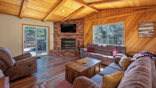Ein Ferienhaus-Innenraum mit Kamin aus Ziegelsteinen, Holzbalkendecke, Ledersessel, Sofa und Fernseher.