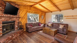 Ein gemütliches Wohnzimmer mit Kamin aus Backstein, Holzbalkendecke und großen Fenstern.