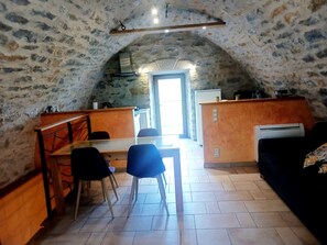 An attic-style room with a dining table, chairs, a sofa, and a kitchen area with a stove and refrigerator.