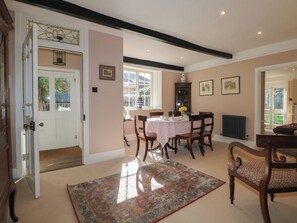 A dining area with a table set for four, surrounded by chairs, a patterned rug, and a window with a view of greenery. - Rectory Cottage (Alton)