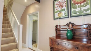 A staircase with beige carpet, a wooden cabinet with a green vase, and two framed botanical prints on the wall. - Rectory Cottage (Alton)