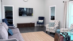 Un salon doté d’un ventilateur de plafond, d’un téléviseur à écran plat, d’une horloge et d’une fenêtre avec des rideaux.