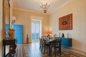A dining area with a chandelier, a blue door, a large window, and a decorative wall piece.