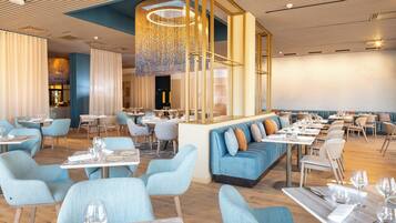 Interior de un restaurante moderno con asientos tapizados en azul, mesas de madera y una lámpara decorativa en el centro.