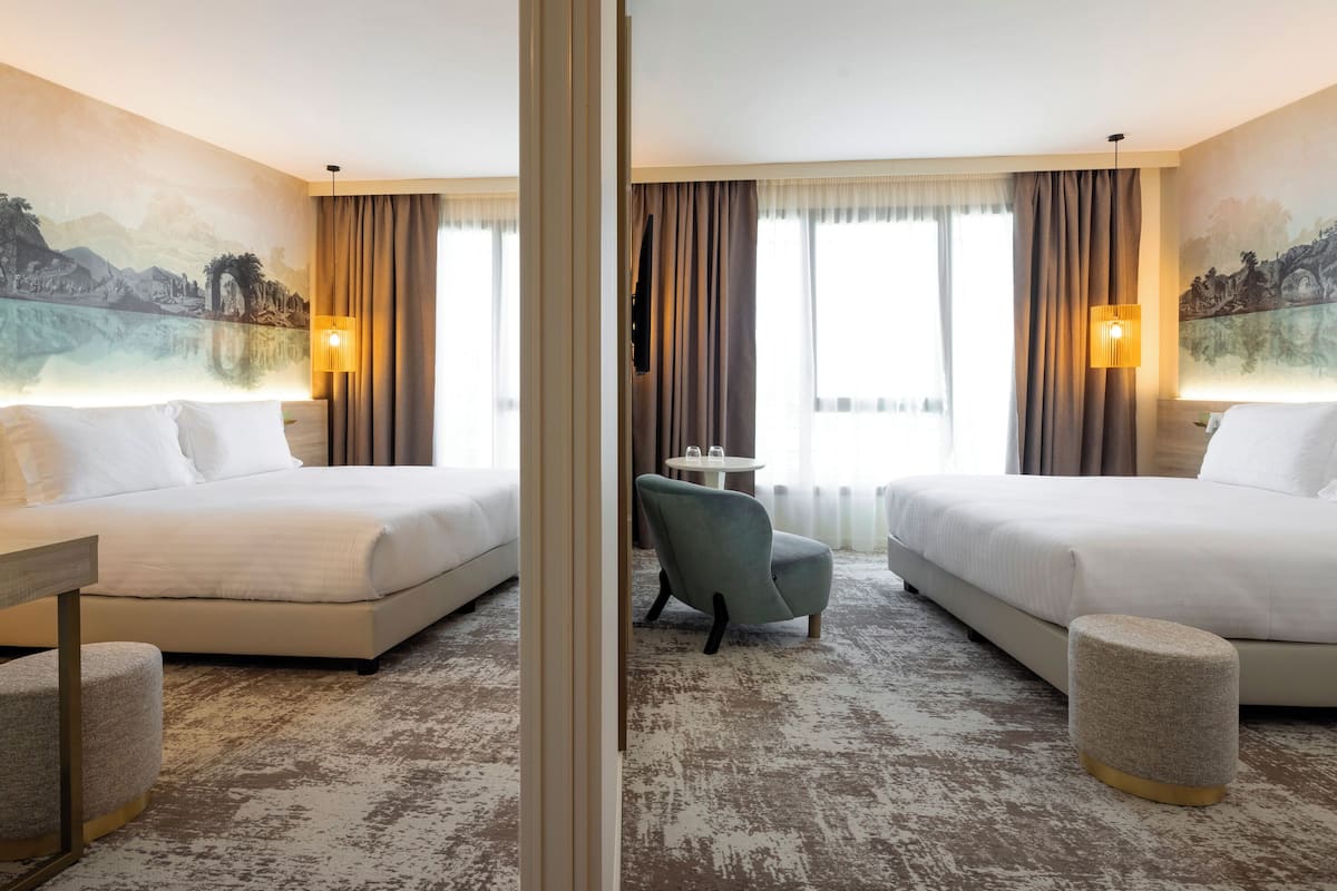 A hotel room with two beds, a small table, a chair, and a lamp.