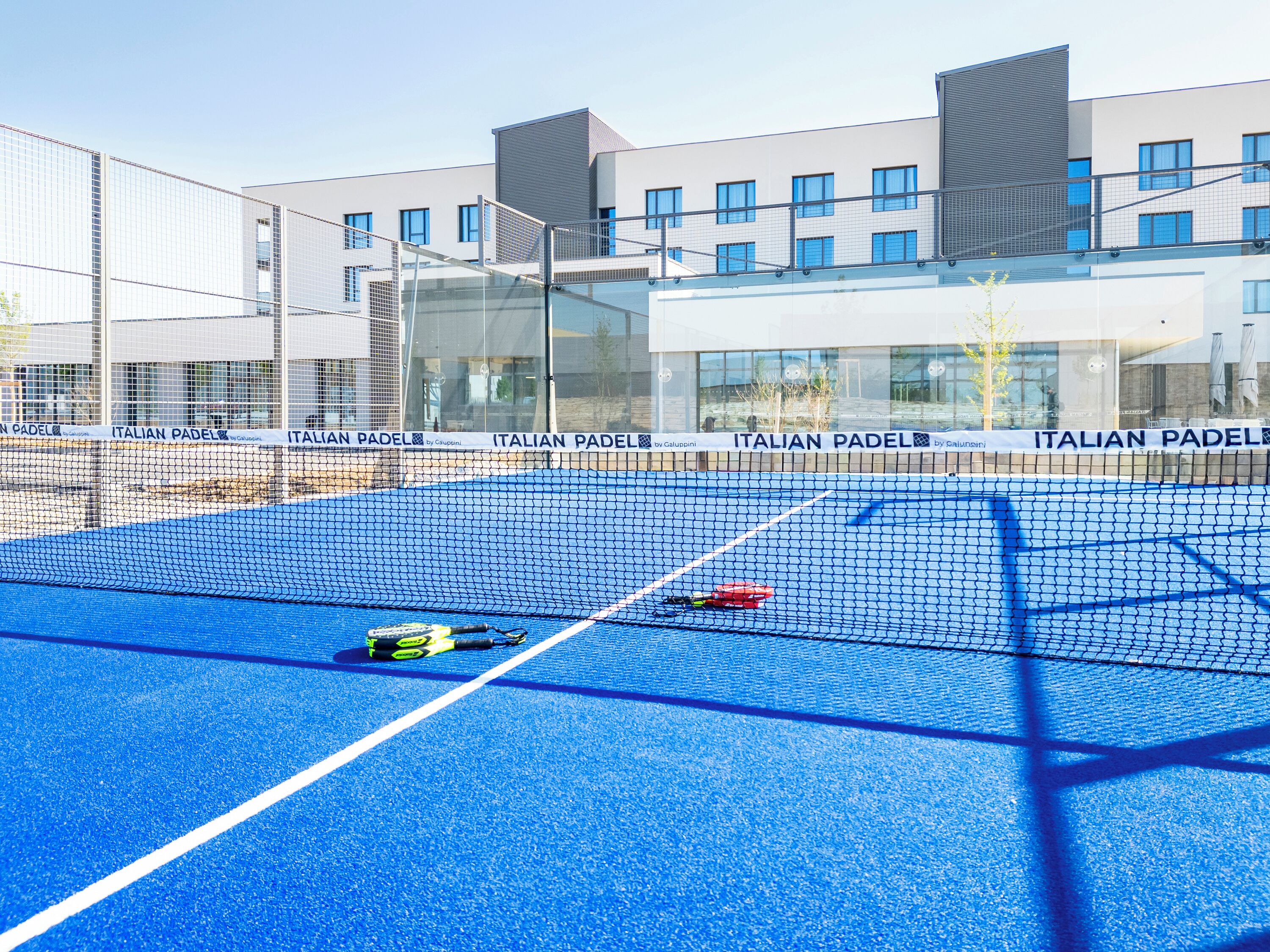 Una cancha de tenis con red, rodeada de edificios modernos con fachadas de vidrio.