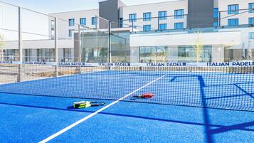 Una cancha de tenis con red, rodeada de edificios modernos con fachadas de vidrio.
