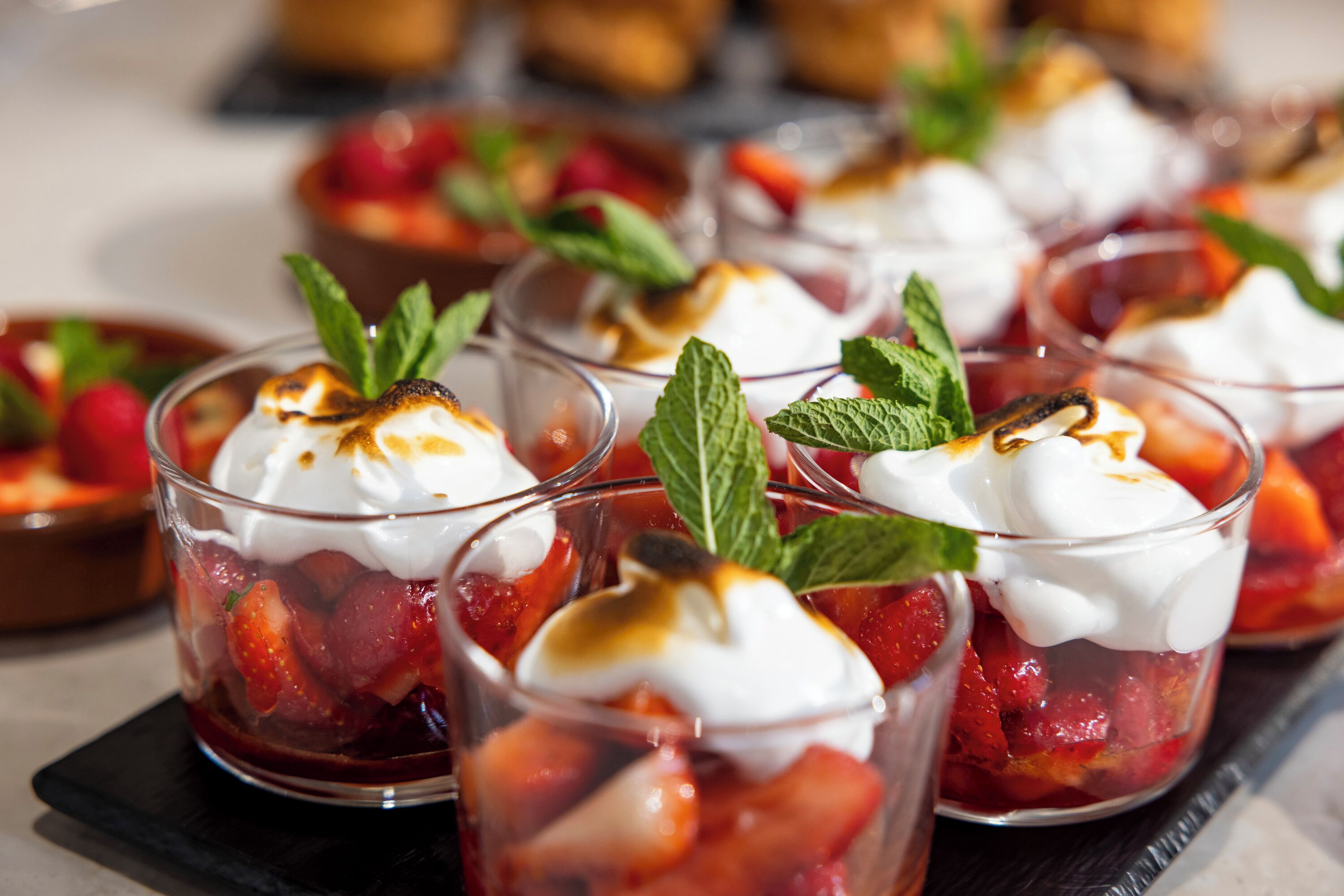 Een rijk gevulde dessertplateau met porties aardbeienparfaits, afgemaakt met slagroom en muntblaadjes.