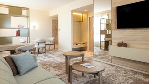 A modern hotel room with a sofa, a small table, a TV, and a bookshelf. - Parkest Hôtel & Spa (Genas)
