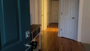 Un pasillo con piso de madera, puertas blancas y una puerta de metal con cerradura.